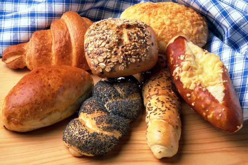 Various German bread rolls and baked goods on a wooden table, including poppy seed rolls, multigrain rolls, pretzels and croissants.