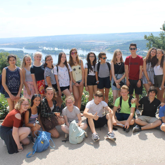 Группа школьников на экскурсии с видом на речной пейзаж и городской пейзаж летом.