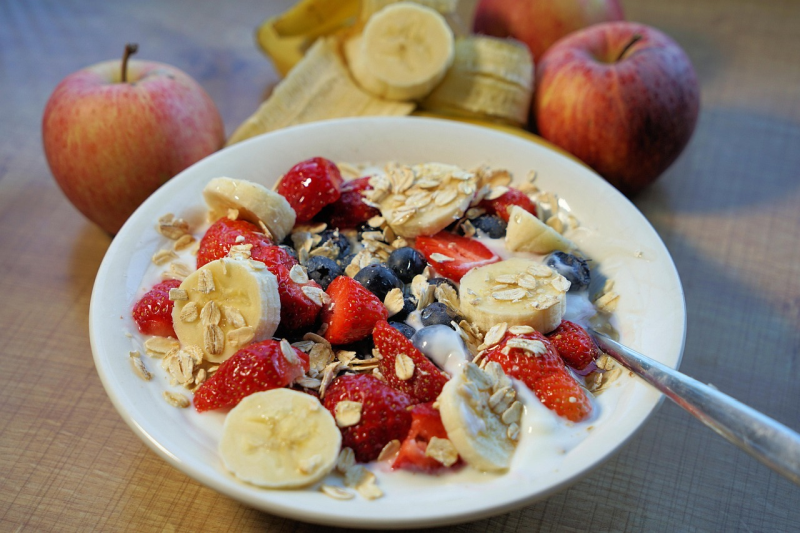 Bowl of muesli with yoghurt, strawberries, blueberries, banana and oatmeal on a table.