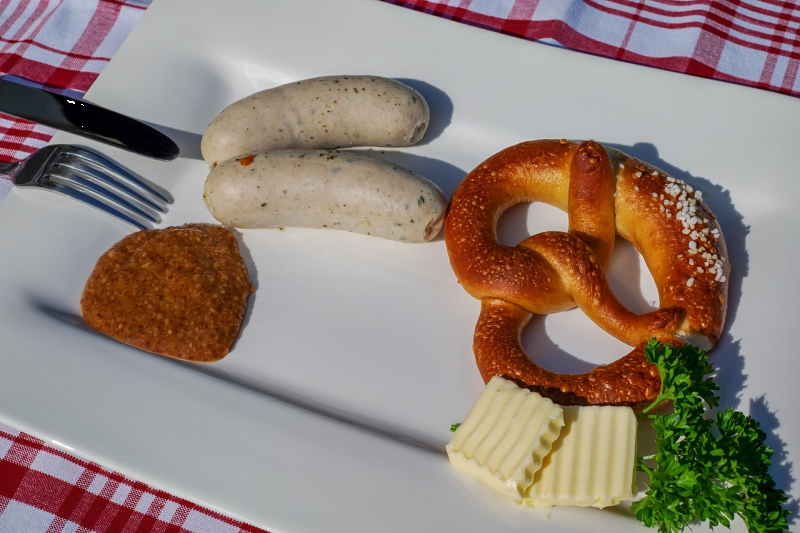 Traditional Bavarian breakfast with white sausage, pretzel, sweet mustard and butter on a plate.